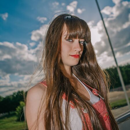 A beautiful girl with long hair coquettishly smiling. Young modern city woman look to the camera. Urban lifestyle holidays.の写真素材