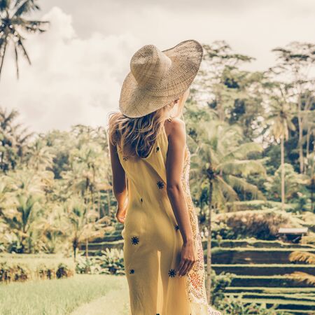 Beautiful young woman in shine through dress and straw hat. Girl walk at typical Asian hillside with rice farming, mountain shape green cascade rice field terraces paddies. Ubud, Bali, Indonesia.の写真素材