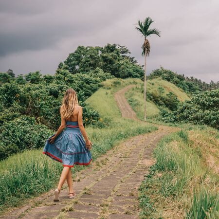 Beautiful young lady in blue vintage dress walking by stone hill path in Asia. Girl travel and explore world. Long lonely road in mountains. Travel and adventure mockup. Romantic scene concept.の写真素材