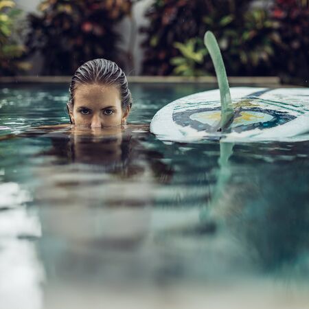 Beautiful cute woman in sexy bikini in pool with her longboard single fin surfing board look to camera like panther. Girl travel and explore world. Travel and adventure mockup. Romantic scene concept.の写真素材