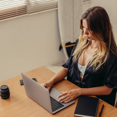 Beautiful young surfer woman in sexy black pajamas work with laptop at home. Happy girl working online, study and learn with notebook computer. Modern business lady, freelance work from home concept.の写真素材