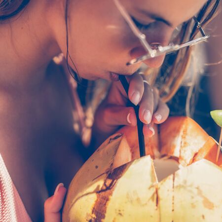 Surfer woman in sexy bikini drink coconut after have fun on big waves in open ocean with surf longboard. Modern active lifestyle, people water sport adventure camp and extreme swim on summer vacation.の写真素材