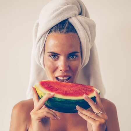 Portrait of beautiful cute woman in sexy lingerie with white towel on head eat slice of juicy red watermelon. Healthy eating lifestyle concept. Health care and beauty. Fitness food. Proper nutrition.の写真素材
