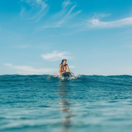 Beautiful sporty surfing girl in sexy bikini on surf longboard surfboard board on sunrise or sunset in the ocean. Woman paddle to catch good wave. Modern active sport lifestyle and summer vacation.の写真素材