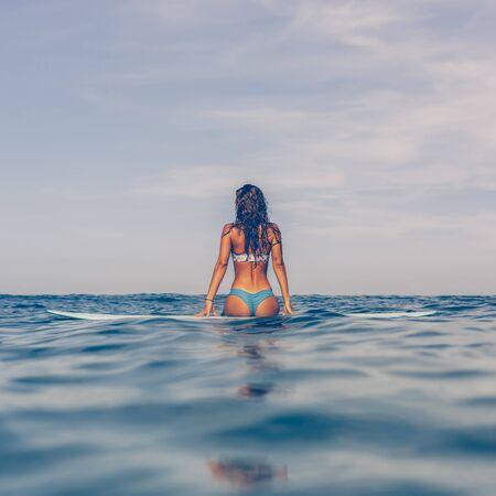 Beautiful sporty surfing girl in sexy bikini swimwear sit on big longboard surf surfboard board on sunrise or sunset and feel unity with the sea. Modern active sport lifestyle and summer vacation.の写真素材