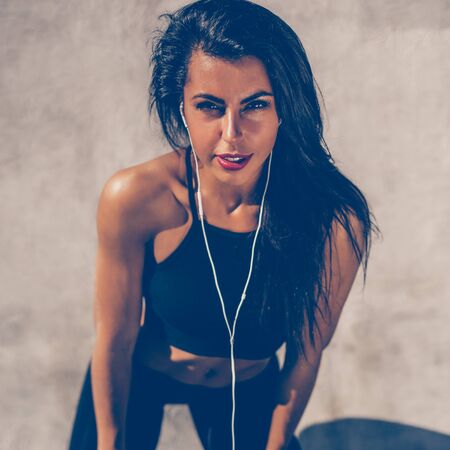 Beautiful strong woman in black sexy leggings with pretty athlete muscular body listen music with headphones. Crossfit training urban area street gym city workout exercise routine healthy lifestyle.の写真素材
