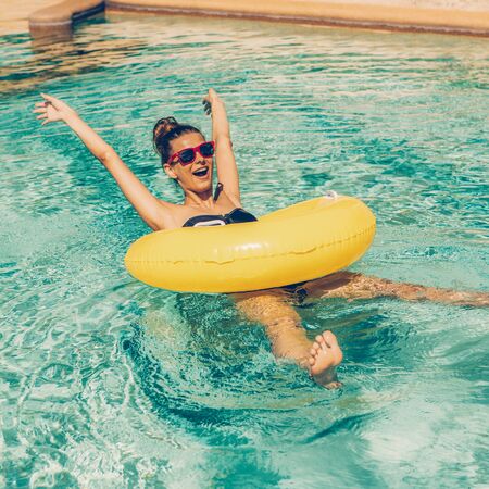 Amazing beautiful lady in swimsuit and sunglasses have fun at swimming pool party. Portrait of sexy girl enjoying hot day, having fun with inflatable ring in water and show her feet and waving hands.の写真素材