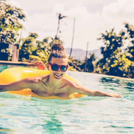 Amazing beautiful lady in sunglasses have fun in swimming pool. Outdoor lifestyle portrait of hipster girl smiling to the camera enjoying summer holidays, swimming with inflatable yellow ring.の写真素材