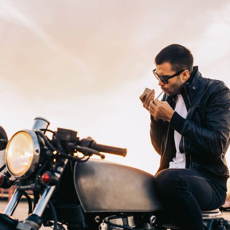 Handsome rider male with beard and mustache in black biker jacket and fashion sunglasses smoke...