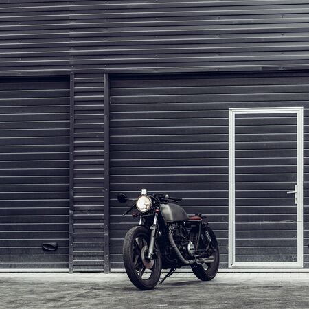 Custom motorcycle parking near dark industrial building. Everything is ready for having fun driving the empty road on a motorcycle tour journey. Hipster city hobby. Space for your individual text.の写真素材