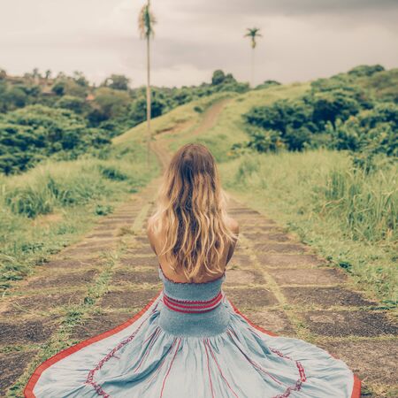 Beautiful young woman in blue vintage dress seat at stone hill path in Asia. Girl travel and explore world. Long lonely mountain road. Travel and adventure mockup. Romantic scene concept. Symmetry.の写真素材