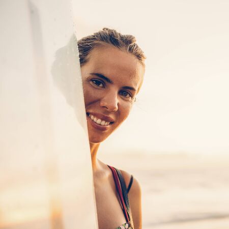 Portrait of young surfer woman in sexy bikini with surfing longboard pose to camera at sunset ocean. Modern family lifestyle, people water sport adventure camp and extreme swim on summer vacation.の写真素材