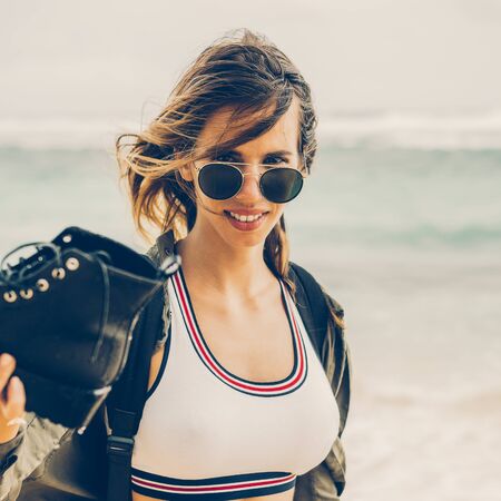 Hipster fit woman in sexy shorts, khaki shirt, sunglasses and travel backpack show her army boots with water. Modern tourist traveler, active lifestyle, sport adventure camp and extreme on vacation.の写真素材