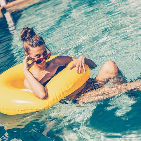 Amazing beautiful female in bikini correct sunglasses and have fun in swimming pool party. Outdoor portrait of sexy girl looking to the camera enjoying summer holidays, swim with inflatable ring.の写真素材