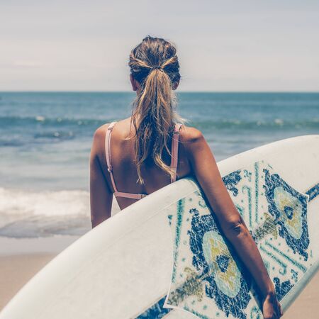 Beautiful young slim girl in sexy pink bikini with long custom surfing board single fin in front of blue ocean ready to surfing. Tropic island vacation. Summer travel girl, active hipster lifestyle.の写真素材
