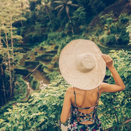 Beautiful young female in straw hat travel and explore world. Girl look at typical Asian hillside with rice farming, mountain shape green cascade rice field terraces paddies. Ubud, Bali, Indonesia.の写真素材