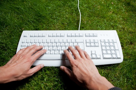 hands typing keyboard on the green grassの写真素材