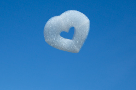 abstract foam shaped heart symbol on blue sky backgroundの写真素材