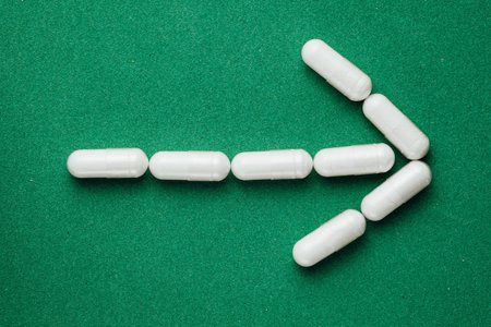 arrow sign of white capsules pills on green backgroundの写真素材