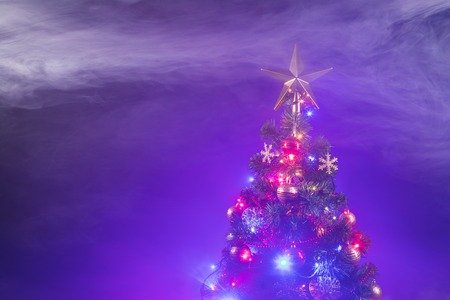 Christmas tree with festive lights, purple background with smokeの写真素材