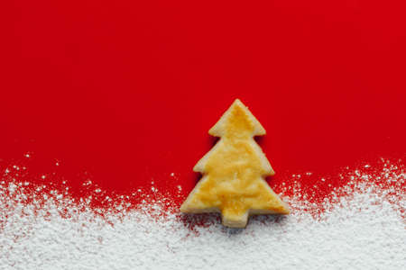 Christmas tree cookie and floury snow, red paper background