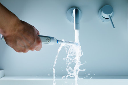 hand holding toothbrush under flowing water from faucet in a bathroom