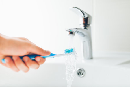 hand holding toothbrush under flowing water from faucetの写真素材