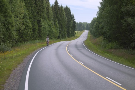 lone cyclist riding along the edge of the winding road in the forestのeditorial素材