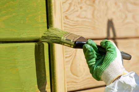hand with a paint brush painting wooden wall in green outdoor shotの写真素材