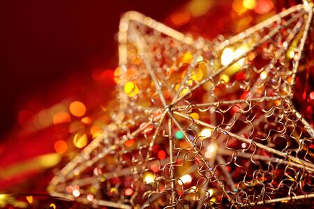 hristmas golden star close-up with blurred lights on red backgroundの写真素材