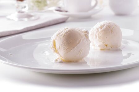 two ice cream scoops on white plate close-up against decorated tableの写真素材