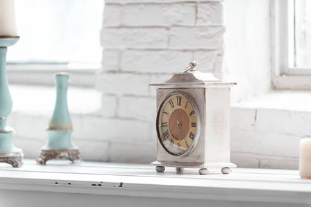 light shabby chic  interior fragment with clock and candlesticks on white brick wall backgroundの写真素材