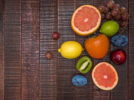 Fresh fruits on a wooden table. Lemon, lime, persimmon, apple, grapefruit, plum, grapes.の写真素材