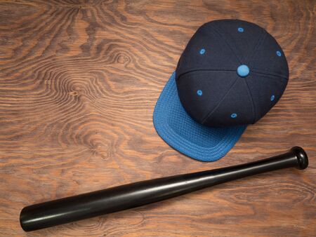 Blue baseball cap and a black bit lie on a wooden tableの写真素材