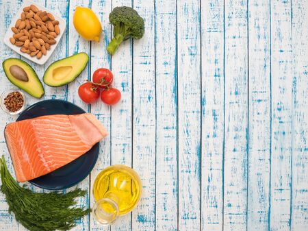 Piece of fresh salmon on a plate, avocado, almonds, sunflower oil and vegetables on a tableの写真素材
