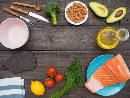 Piece of fresh salmon on a plate, almond nuts, avocado, sunflower oil and vegetables on a wooden tableの写真素材