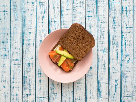 Sandwich with salmon, avocado, cream cheese and black bread in a plate on a wooden tableの写真素材