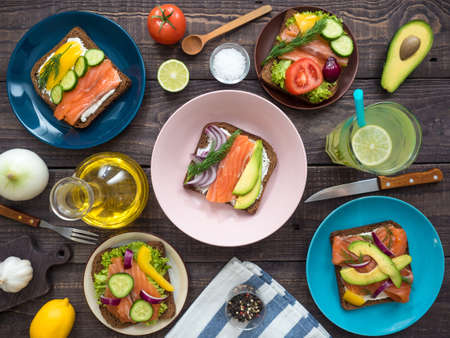 Sandwiches with salmon, cream cheese, black bread, vegetables in plates and a large glass of...