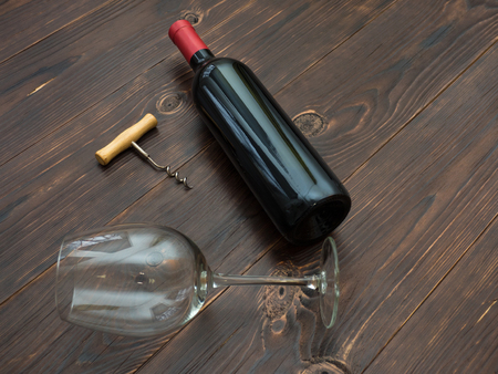 Bottle of red wine, a wooden corkscrew and a glass lie on an old tableの写真素材