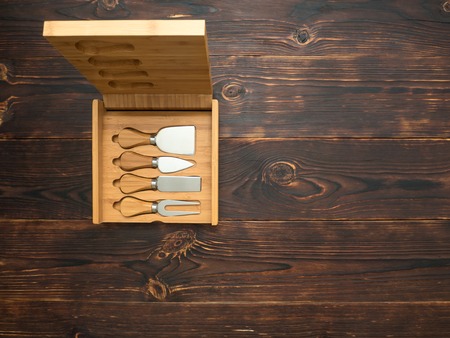 Sharp and new knives for cheese with wooden handles lie in a box on the table