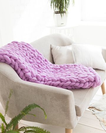 A large merino lilac plaid blanket lies on a sofa. Coarse violet plaid of merino wool. Plaid. Cozy interior. Handmadeの写真素材