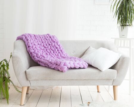A large merino lilac plaid blanket lies on a sofa. Coarse violet plaid of merino wool. Plaid. Cozy interior. Handmadeの写真素材