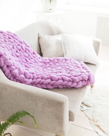 A large merino lilac plaid blanket lies on a sofa. Coarse violet plaid of merino wool. Plaid. Cozy interior. Handmadeの写真素材