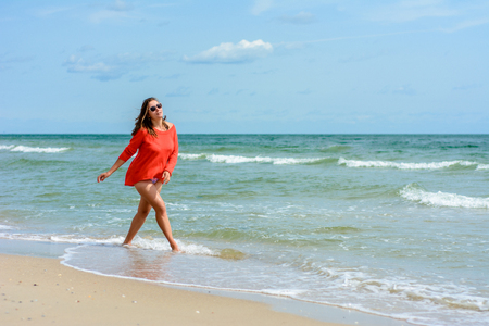 A charming woman walks on the Black Sea coast. A young brunette poses on a beach in a red lilyの写真素材