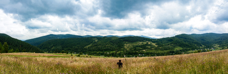The guy is sitting on a green mountain and enjoys an enchanting view. Amazing Panorama of Ukrainian Carpathiansの写真素材