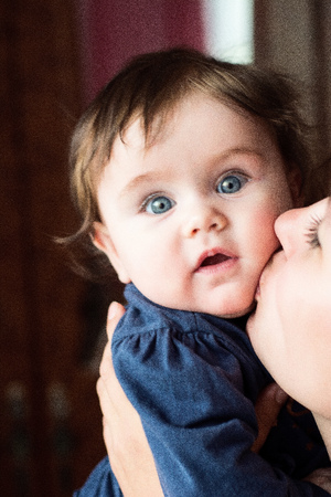 A wonderful baby is enchantingly looking at us during a mom's kissの写真素材