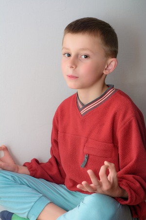 A cute boy sits in a red jacket with an isolated backgroundの写真素材