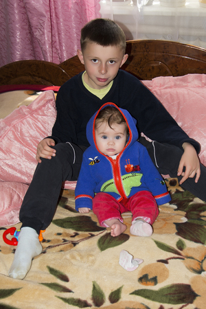 Little brother and sister are sitting on the bed in the roomの写真素材