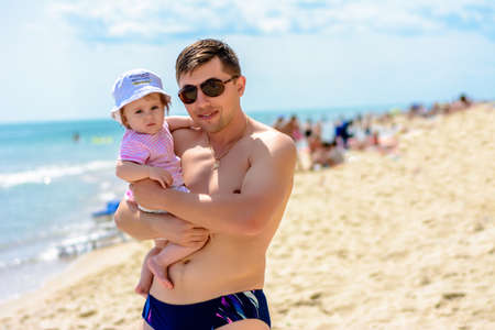 Little beautiful girl in a hat and pink dress is playing with her father on the beach.の写真素材