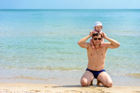 Young father in glasses sits on the beach with his daughterの写真素材
